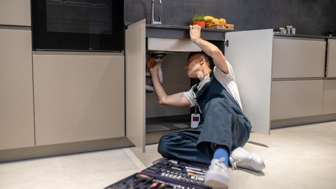 Un homme répare un évier dans une cuisine, illustrant des solutions de plomberie résidentielle fiables pour le confort de la maison.