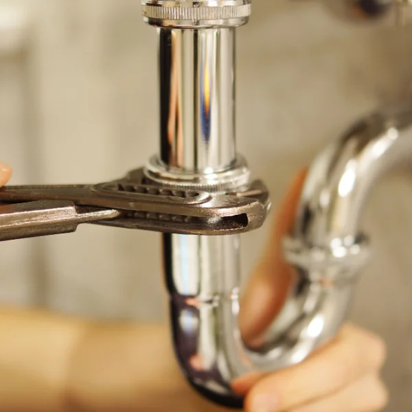 A person uses pliers to repair a pipe, demonstrating a hands-on approach to plumbing maintenance.